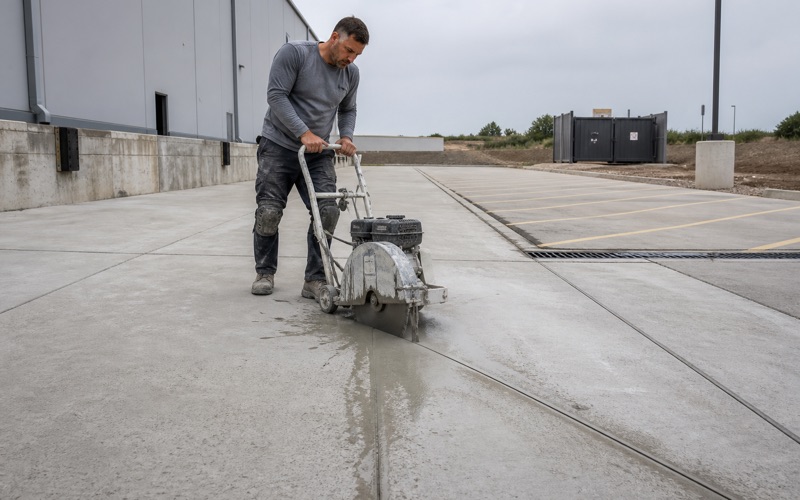 A walk-behind saw cutting control joints across a commercial slab in Killeen, with slurry trailing behind and a loading dock apron beyond.